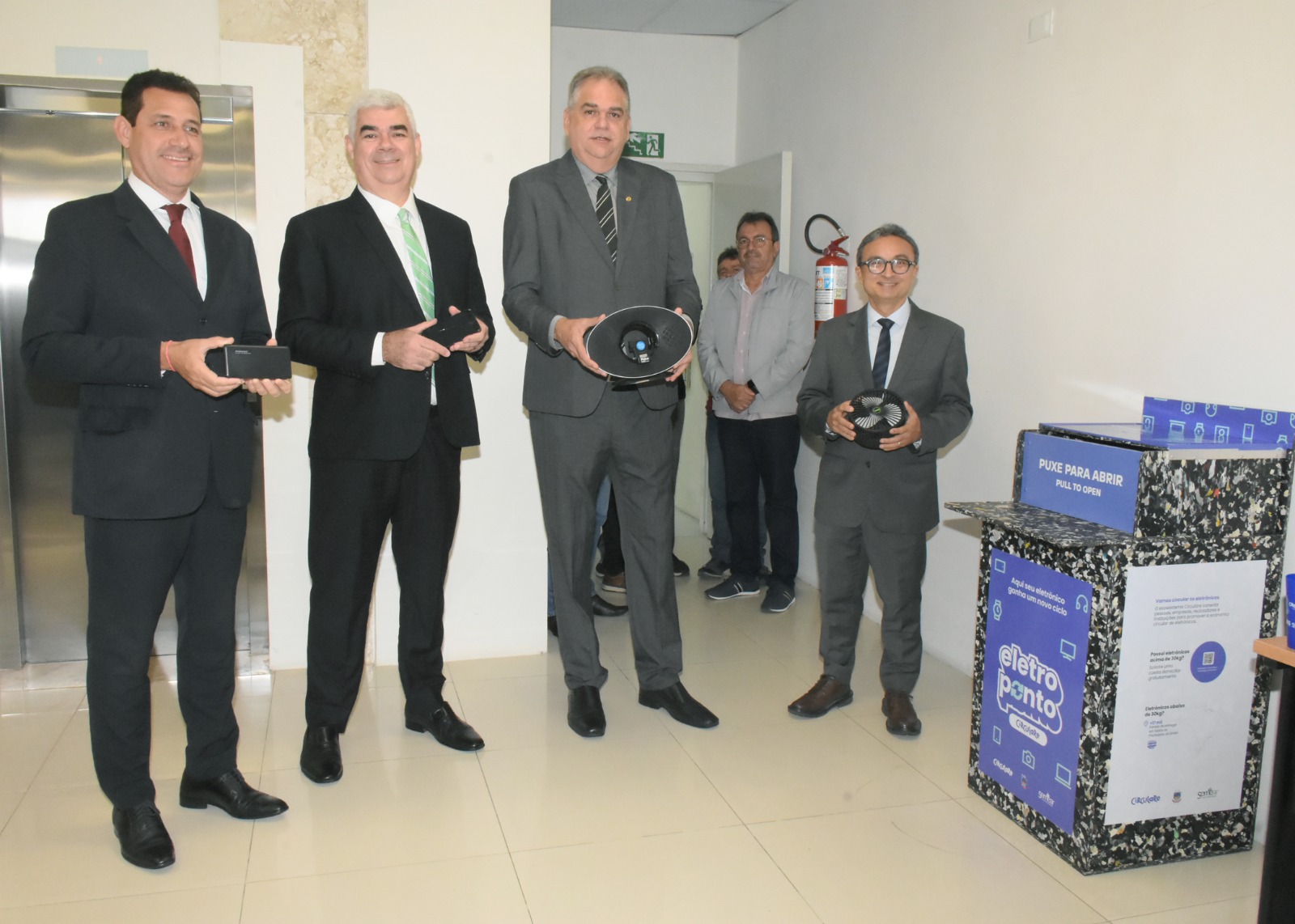 Presidente do TJ ao lado dos auxiliares em frente a urna coletora de eletrônicos